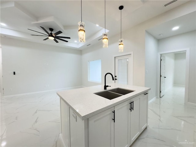 kitchen with pendant lighting, sink, white cabinets, a tray ceiling, and a center island with sink