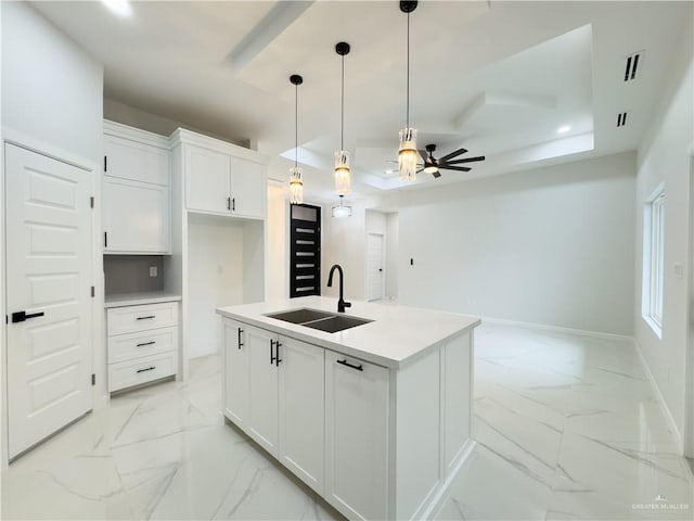 kitchen with sink, white cabinets, a kitchen island with sink, ceiling fan, and a raised ceiling