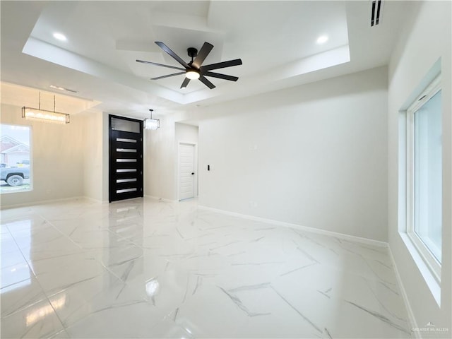 unfurnished room with a raised ceiling and ceiling fan with notable chandelier