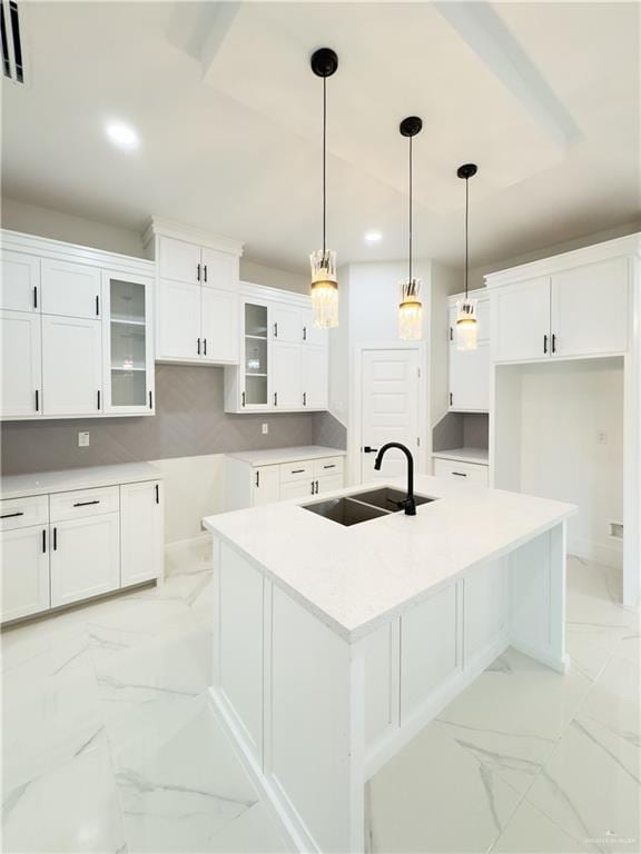 kitchen with hanging light fixtures, an island with sink, sink, and white cabinets