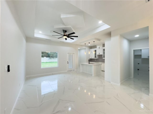 unfurnished living room featuring ceiling fan, a tray ceiling, and sink