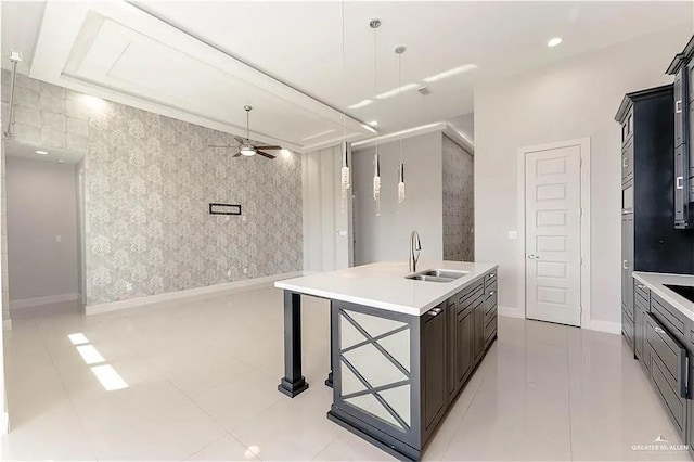 kitchen with a breakfast bar, ceiling fan, a kitchen island with sink, sink, and pendant lighting