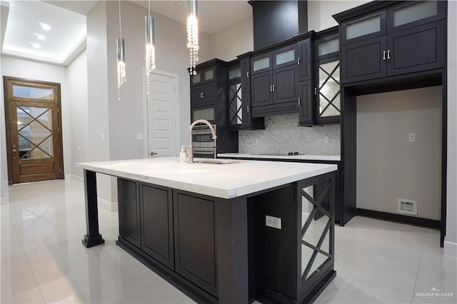 kitchen featuring a breakfast bar, backsplash, a kitchen island with sink, sink, and hanging light fixtures