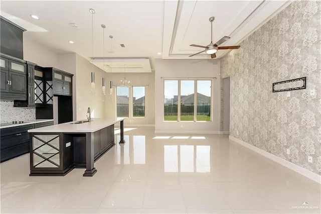 kitchen with a kitchen breakfast bar, ceiling fan with notable chandelier, sink, an island with sink, and light tile patterned flooring