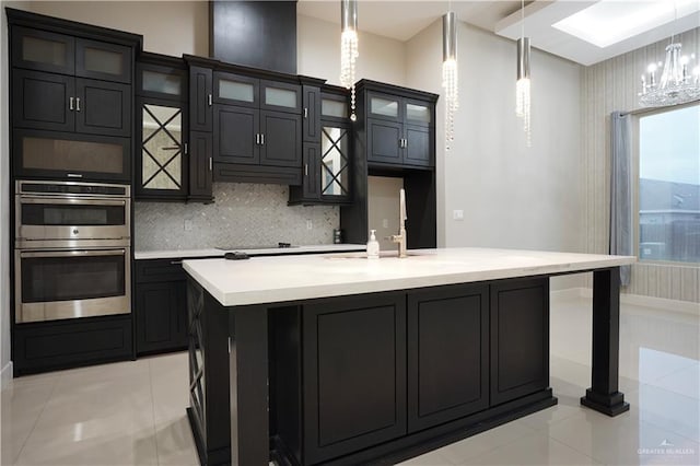 kitchen featuring decorative backsplash, a center island with sink, pendant lighting, and a notable chandelier