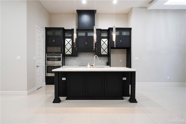 kitchen with tasteful backsplash, light tile patterned floors, sink, and an island with sink