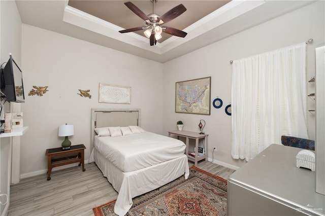 bedroom with ceiling fan, ornamental molding, light hardwood / wood-style flooring, and a raised ceiling