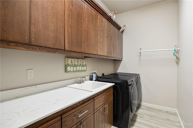 clothes washing area with independent washer and dryer, sink, light hardwood / wood-style floors, and cabinets