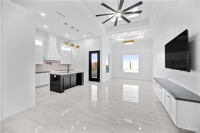 kitchen featuring a center island with sink, a raised ceiling, open floor plan, custom exhaust hood, and a sink