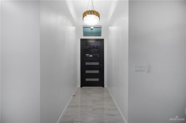 doorway to outside featuring marble finish floor, baseboards, and an inviting chandelier