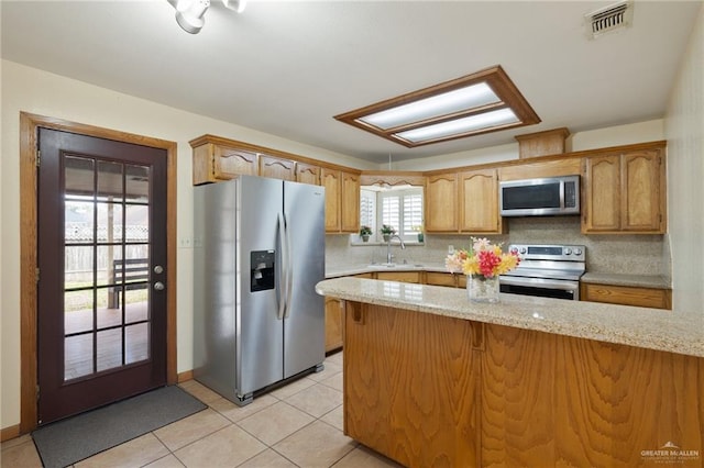 kitchen with tasteful backsplash, stainless steel appliances, light stone counters, light tile patterned flooring, and sink