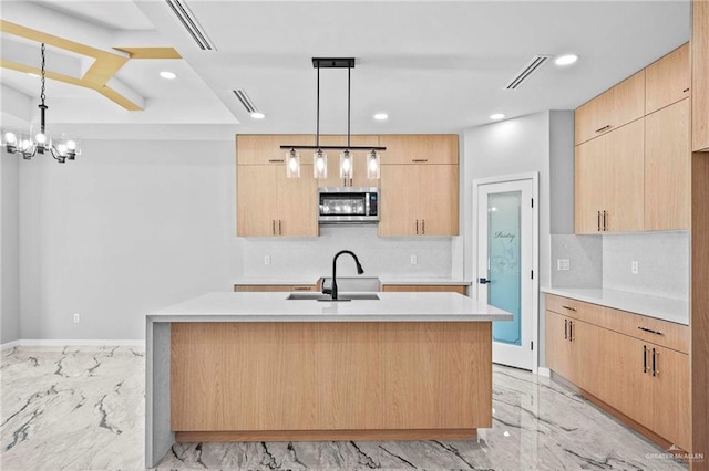 kitchen with decorative backsplash, light brown cabinetry, hanging light fixtures, and a center island with sink