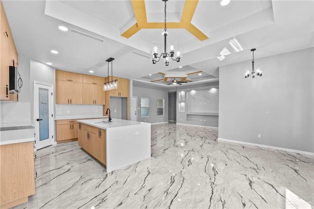 kitchen featuring sink, a raised ceiling, decorative light fixtures, a center island with sink, and ceiling fan with notable chandelier