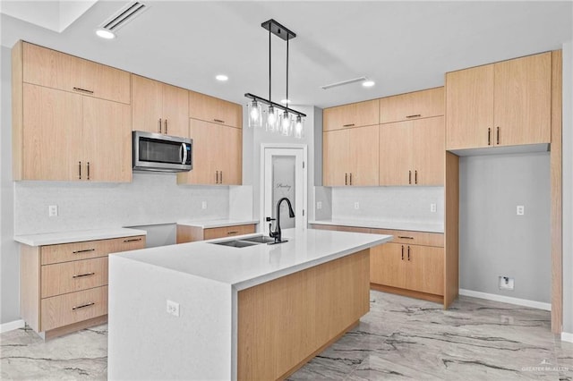 kitchen with decorative light fixtures, an island with sink, and light brown cabinetry