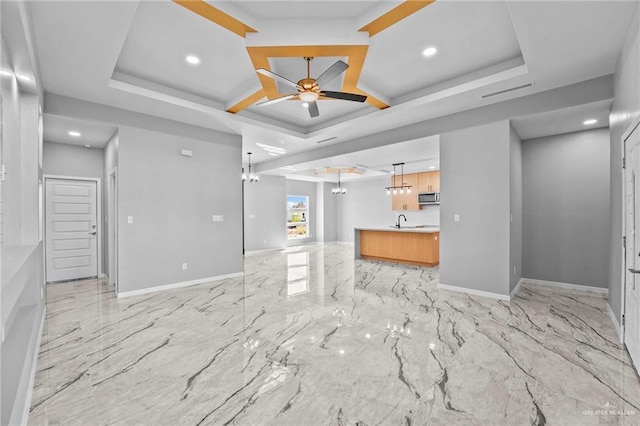 unfurnished living room with a raised ceiling, ceiling fan, and sink