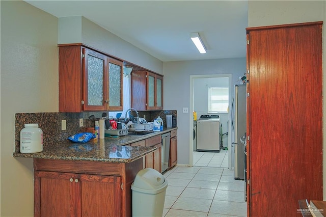 kitchen with washer / dryer, stainless steel appliances, dark stone countertops, sink, and light tile patterned floors