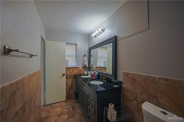 bathroom featuring tile walls, toilet, vanity, and a textured ceiling