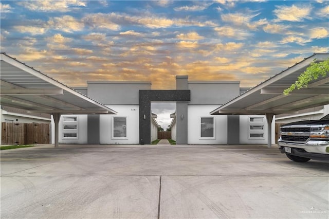 modern home with stucco siding, covered parking, and fence