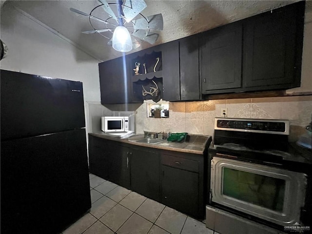 kitchen with light tile patterned floors, electric range, white microwave, freestanding refrigerator, and a sink