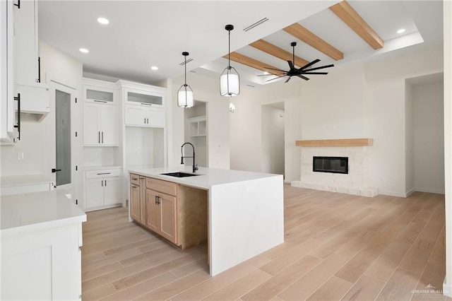 kitchen featuring a center island with sink, white cabinets, sink, decorative light fixtures, and light hardwood / wood-style floors