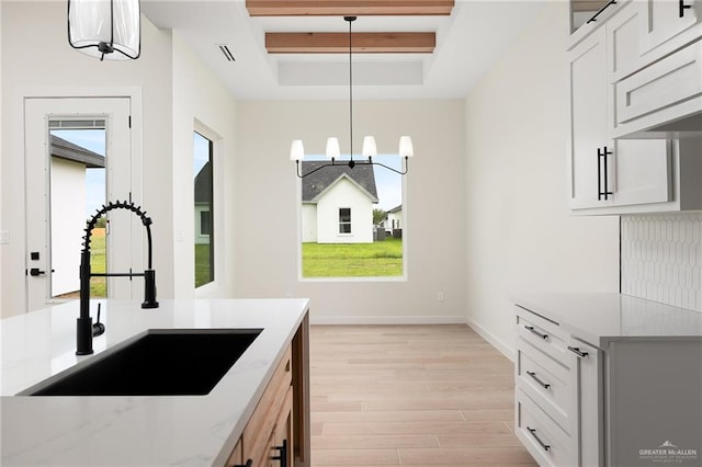 kitchen with a raised ceiling, sink, decorative light fixtures, a notable chandelier, and light hardwood / wood-style floors