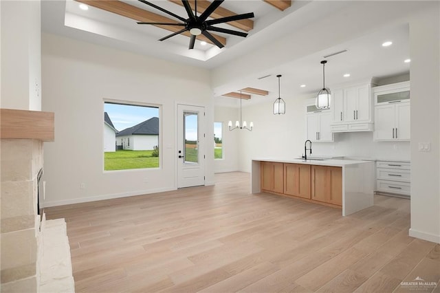 kitchen with a center island with sink, decorative light fixtures, white cabinetry, and light hardwood / wood-style flooring