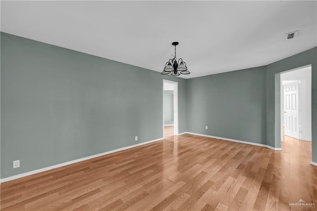 spare room with an inviting chandelier and light hardwood / wood-style floors