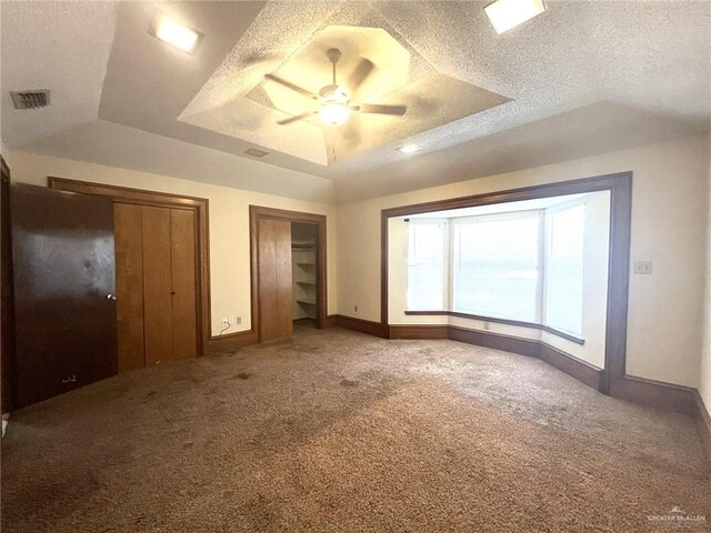 unfurnished bedroom with ceiling fan, a raised ceiling, light colored carpet, a textured ceiling, and two closets