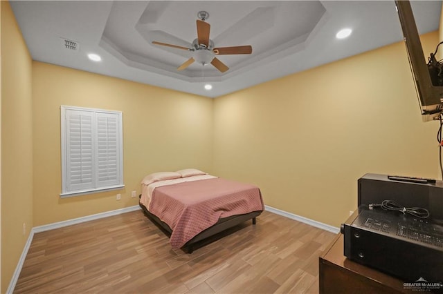 bedroom with a tray ceiling, recessed lighting, baseboards, and wood finished floors