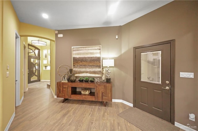 entryway featuring arched walkways, wood finished floors, and baseboards