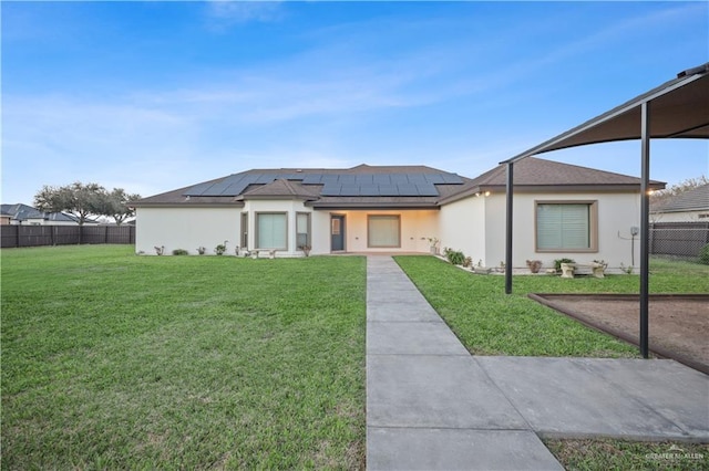 view of front of house with a front yard, fence, roof mounted solar panels, and stucco siding