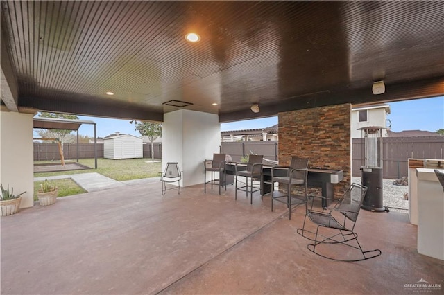 view of patio / terrace featuring a storage shed, a fenced backyard, outdoor dining space, and an outdoor structure