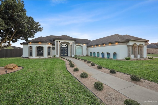 mediterranean / spanish-style home featuring french doors, a front lawn, fence, and stucco siding