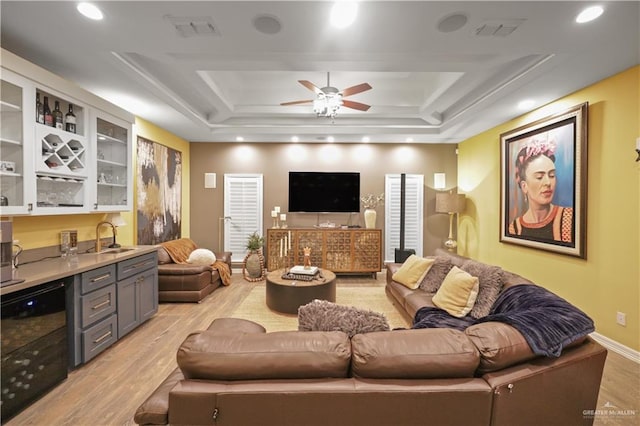 living room featuring a tray ceiling, indoor wet bar, visible vents, and light wood-style floors