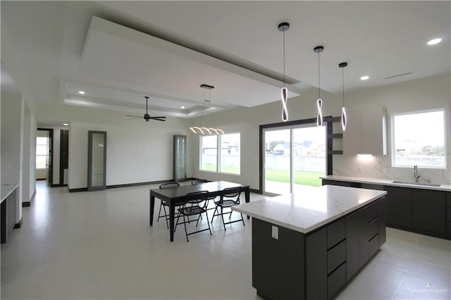 kitchen featuring a large island, sink, ceiling fan, a raised ceiling, and decorative light fixtures