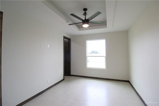 empty room with ceiling fan and a tray ceiling