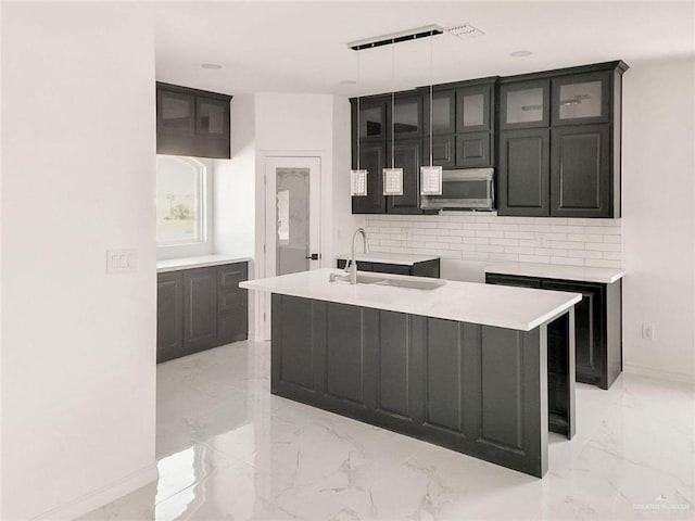 kitchen with pendant lighting, sink, an island with sink, and tasteful backsplash