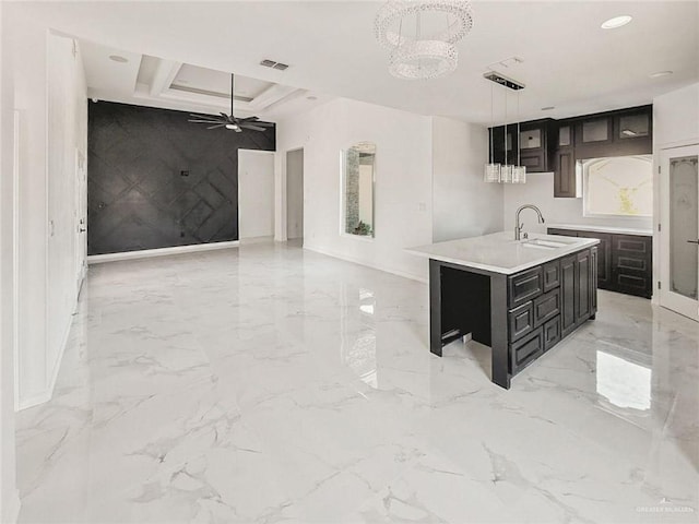 kitchen with decorative light fixtures, sink, ceiling fan with notable chandelier, and an island with sink