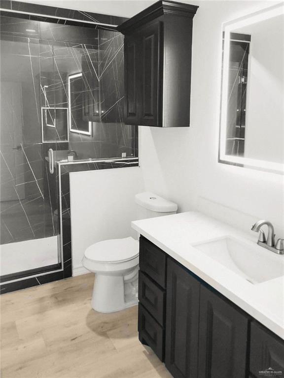 bathroom featuring wood-type flooring, vanity, toilet, and a shower with door