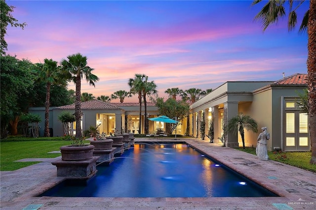 pool at dusk featuring pool water feature and a lawn