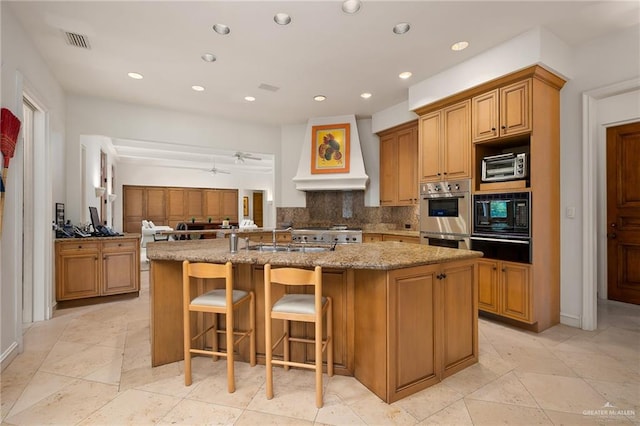 kitchen featuring sink, a kitchen island with sink, premium range hood, a breakfast bar area, and decorative backsplash