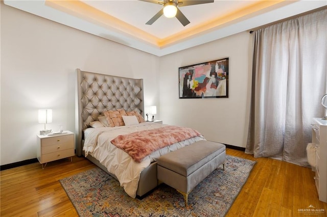 bedroom featuring a raised ceiling, ceiling fan, and light wood-type flooring