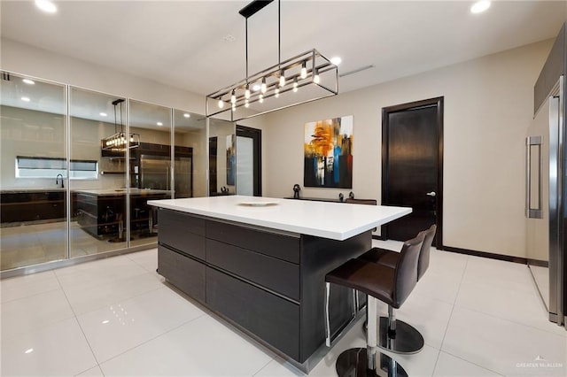 kitchen featuring a breakfast bar area, built in refrigerator, hanging light fixtures, light tile patterned floors, and a kitchen island