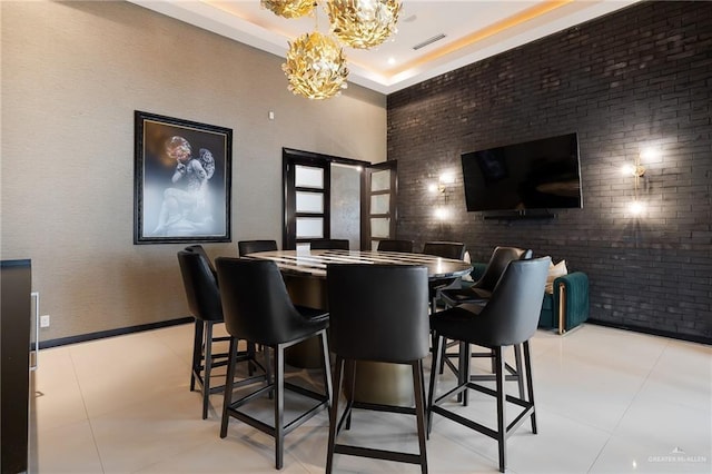 interior space with a notable chandelier, a tray ceiling, brick wall, and a high ceiling