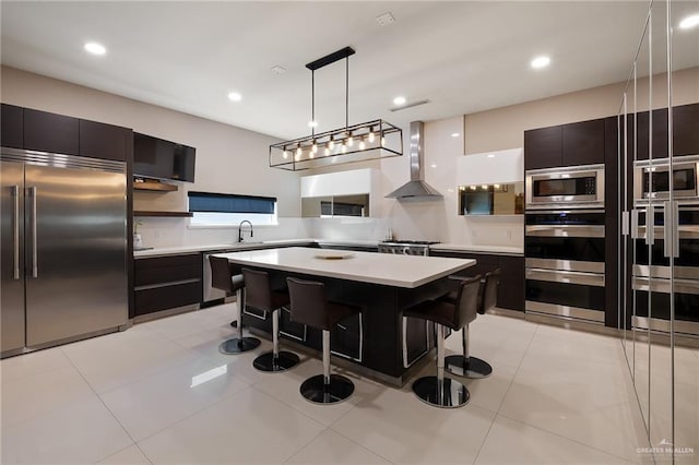 kitchen featuring pendant lighting, a kitchen breakfast bar, a center island, built in appliances, and wall chimney range hood