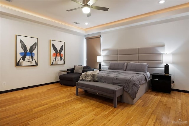 bedroom with ceiling fan, a raised ceiling, and light hardwood / wood-style flooring