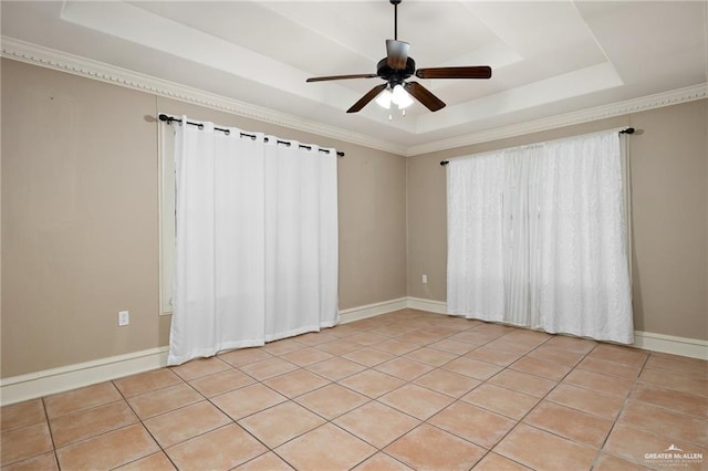 empty room with a raised ceiling, ceiling fan, light tile patterned flooring, and ornamental molding