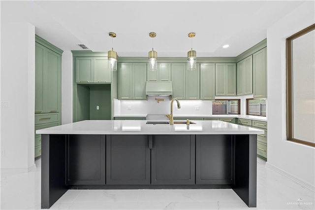 kitchen with sink, hanging light fixtures, green cabinetry, and an island with sink