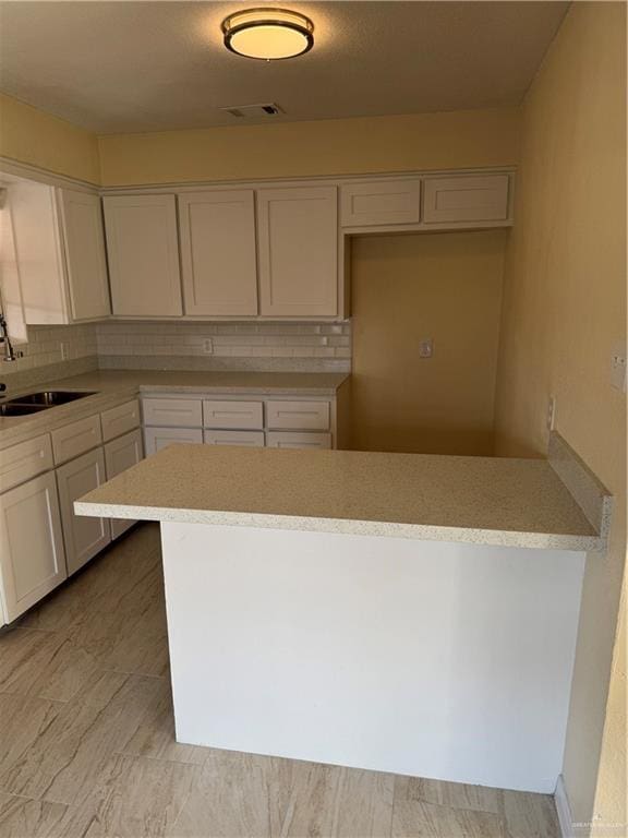 kitchen featuring kitchen peninsula, decorative backsplash, sink, and white cabinets