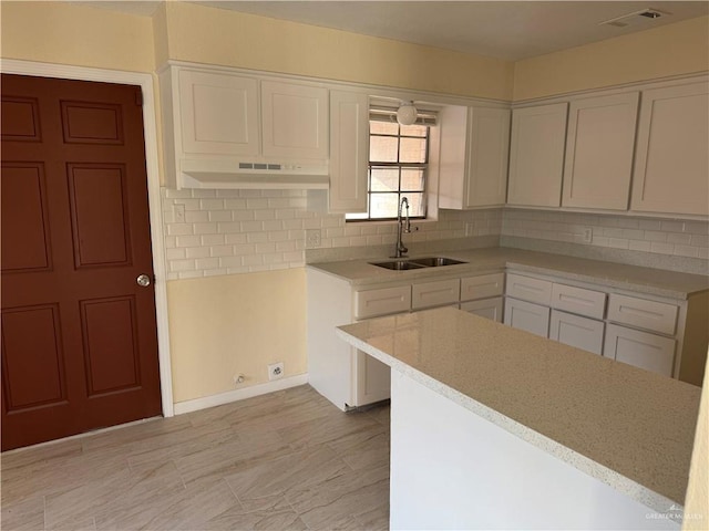 kitchen with decorative backsplash, white cabinetry, sink, and light stone counters